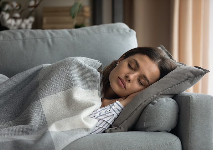 Young woman sleeping on the couch during the day under a blanket