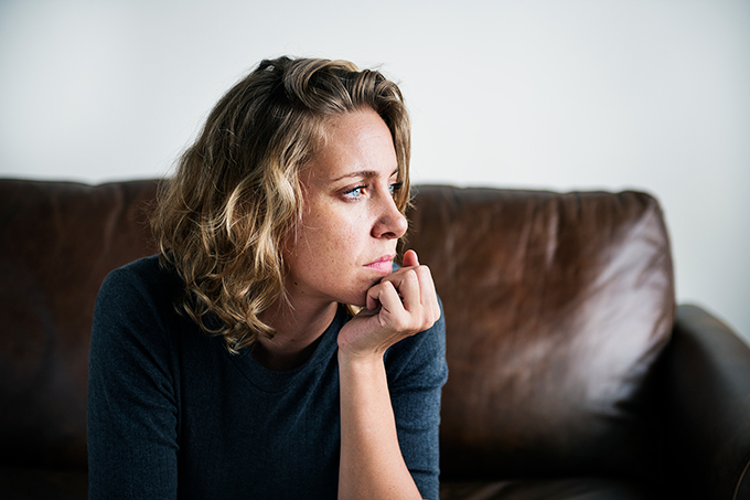Woman sitting on couch at home pensive
