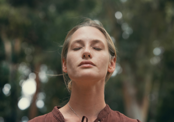 Woman reflecting and taking deep breaths outside with eyes closed